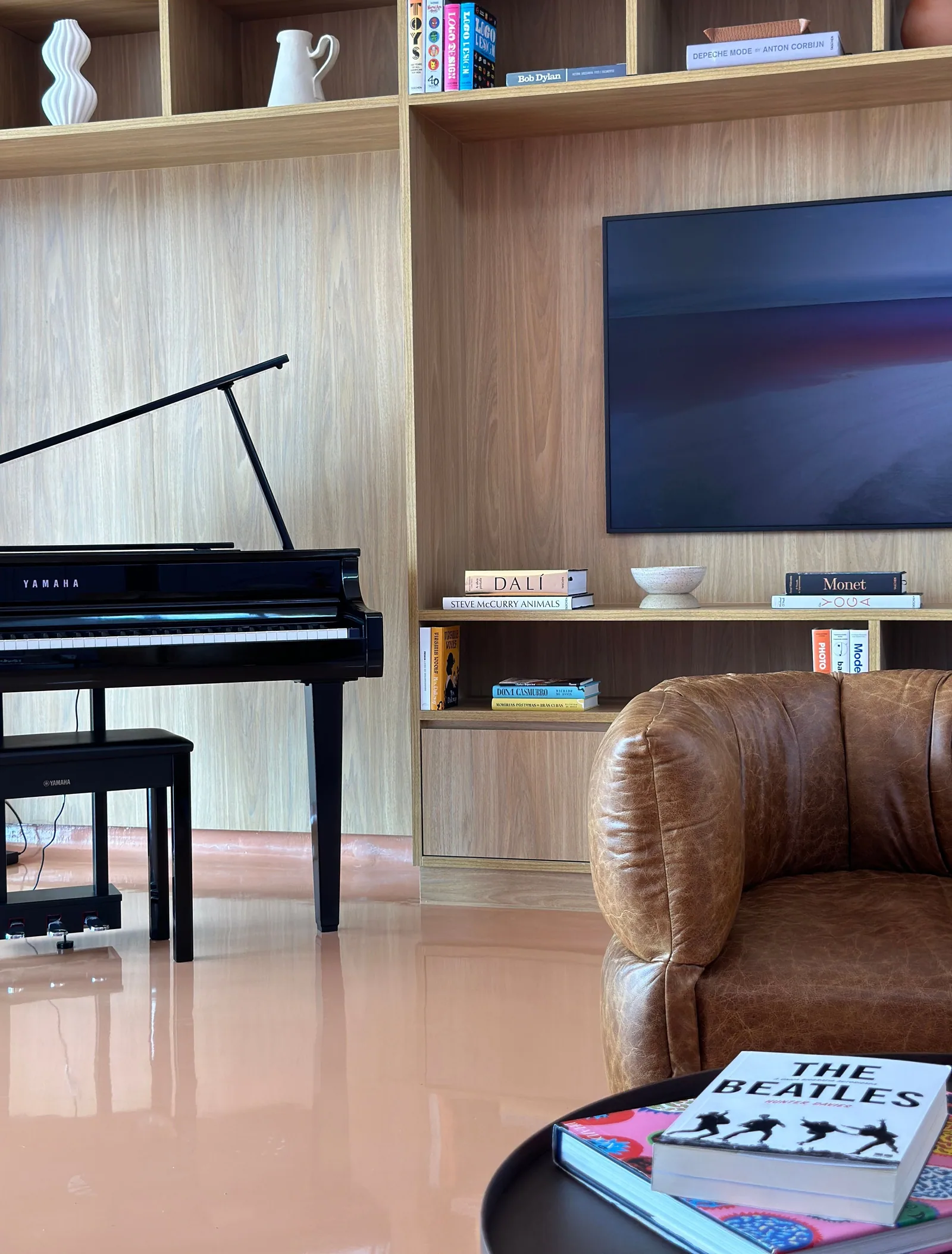 Sala de convivência com piano, estante de livros, TV e poltrona de couro