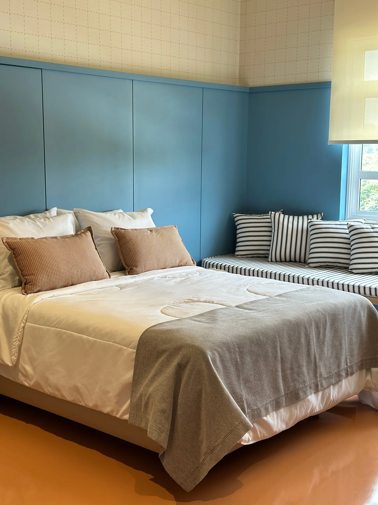 Quarto com cama de casal, parede azul e banco estofado sob a janela